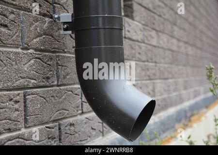 Regenrinne aus Metall fallrohr mit Ankerbolzenhalter an der Hausziegelwand. Stockfoto