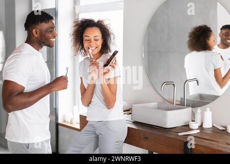 Schwarzes Paar putzt im modernen Badezimmer mit Handy die Zähne Stockfoto