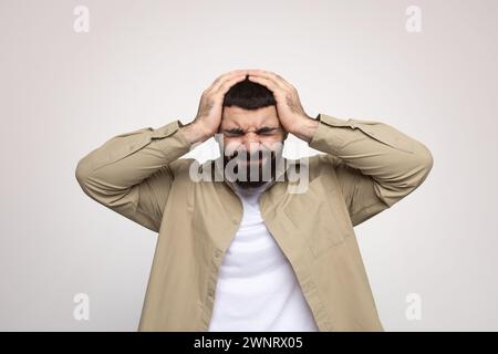 Ein gestresster Mann mit einem Bart, der frustriert und den Kopf in den Händen hält Stockfoto