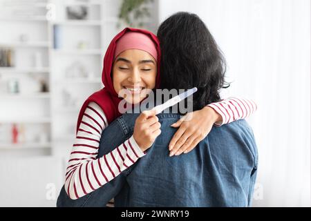 Glücklich Aufgeregte Junge Muslimische Frau Mit Positivem Schwangerschaftstest Und Umarmung Des Ehemanns Stockfoto