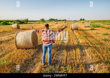 Glücklicher Bauer steht neben Heuballen. Er ist zufrieden wegen der erfolgreichen Ernte. Stockfoto