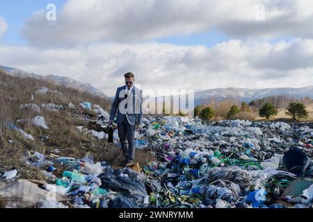 Geschäftsmann, der auf Mülldeponien rüberläuft, großer Müllhaufen. Konsum versus Verschmutzungskonzept. Soziale Verantwortung von Unternehmen im Unternehmen. Stockfoto