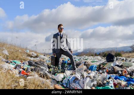 Geschäftsmann, der auf einer Deponie steht, großer Müllhaufen. Konsum versus Verschmutzungskonzept. Soziale Verantwortung von Unternehmen im Unternehmen. Stockfoto