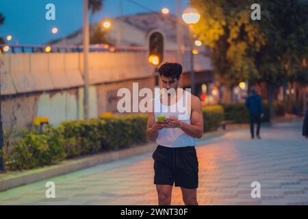 Mann im Tanktop, der nachts das Handy hält Stockfoto
