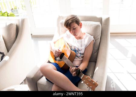 Teen Boy sitzt in Sunshine und lernt Gitarre zu spielen Stockfoto