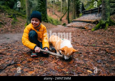 Ein Junge und sein Corgi-Hund spielen zusammen im Wald Stockfoto
