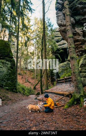 Ein Junge und sein Corgi-Hund spielen zusammen im Wald Stockfoto