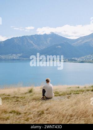 Frau sitzt auf grasbewachsenem Blick auf den blauen See und die wunderschönen Berge Stockfoto