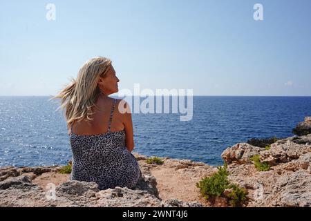 Eine reife Frau, die auf dem Rücken sitzt und auf das Meer blickt. Ruhige Szene im Sommer Stockfoto