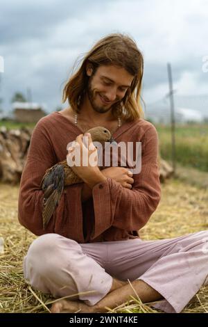 Ein lächelnder langhaariger Mann hält Ente in den Händen. Stockfoto