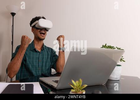 Schwarzer Mann mit VR-Brille bei Remote Job. Junger Nomad auf einem Telearbeit-Meeting am Schreibtisch mit Laptop Stockfoto