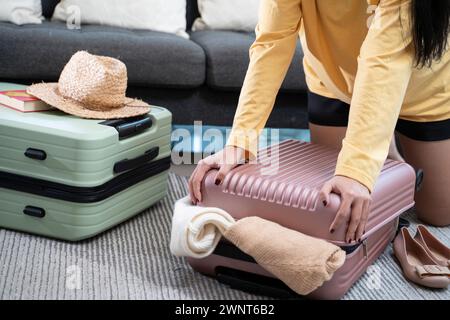 Asiatische junge Frau, die Kleidung stapelt und in einen Koffer steckt, versucht, Handgepäck zu packen. Stockfoto