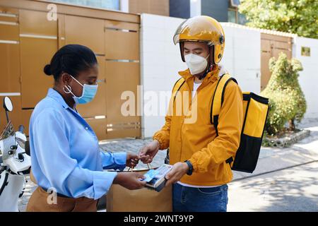 Frau in medizinischer Maske, die für die Lieferung von Lebensmitteln bezahlt Stockfoto