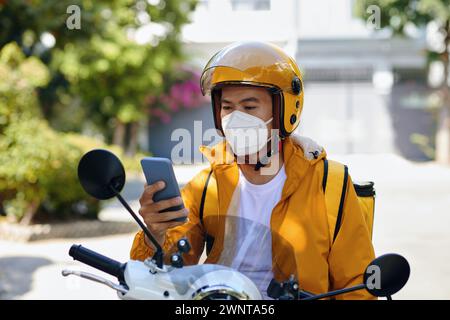 Ernster Liefermann sitzt auf dem Motorrad, wenn er die nächste Bestellbenachrichtigung auf dem Smartphone liest Stockfoto