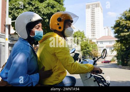 Fröhliche Frau, die medizinische Maske trägt, wenn sie Motorradtaxi-Service benutzt Stockfoto