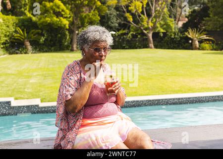 Ältere Frau mit grauen Haaren genießt einen Drink am Pool Stockfoto