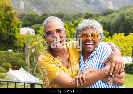 Ältere afroamerikanische Frauen und ältere birassische Frauen teilen sich eine freudige Umarmung im Freien Stockfoto