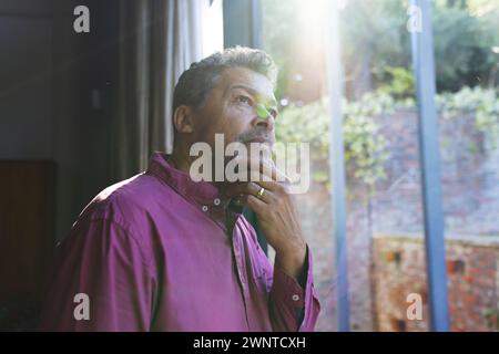 Ein älterer birassischer Mann mit grauen Haaren wirkt nachdenklich, Hand am Kinn, schaut raus Stockfoto