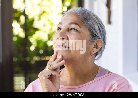 Eine ältere Frau mit grauen Haaren sieht nachdenklich aus und berührt ihr Kinn Stockfoto