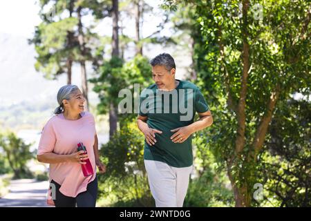 Senior Biracial Pärchen, die zusammen in einem üppigen Park joggen Stockfoto