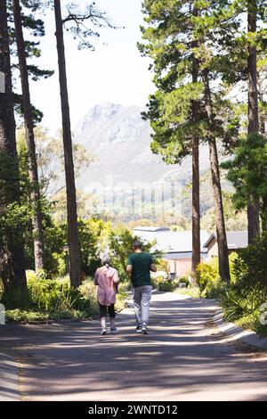 Ältere Frau und Mann laufen auf einer von Bäumen gesäumten Straße, Berge voraus, mit Kopierraum Stockfoto