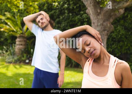 Junge afroamerikanische Frau und kaukasischer Mann dehnen sich in einem sonnigen Garten Stockfoto