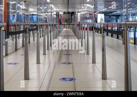 Flughafen Schiphol, Niederlande: Leere moderne U-Bahn-Drehkreuze mit sozialabweisenden Bodenaufklebern und Reflexionen Stockfoto