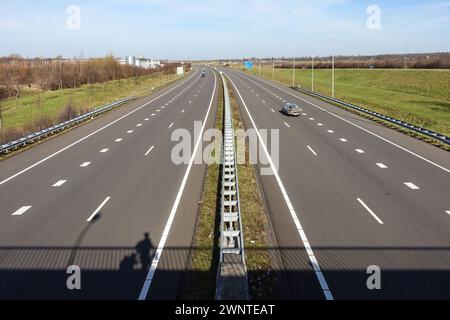 Leere mehrspurige Autobahn mit Verkehr und grünem Mittelstreifen in Limburg in den Niederlanden, mit dem Schatten eines Mannes, der auf einer Brücke steht Stockfoto