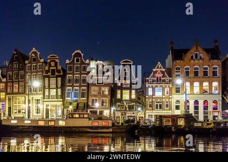 Historische holländische Gebäude, die bei Nacht entlang eines ruhigen Kanals in Amsterdam beleuchtet werden und sich auf der Wasseroberfläche spiegeln. Stockfoto