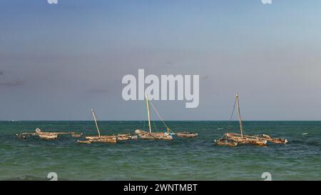 Vier traditionelle hölzerne Ausleger-Dhow-Boote, die bei Flut am Strand von Jambiani, Sansibar, Tansania, vor Anker gehen Stockfoto
