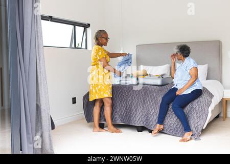 Zwei Seniorinnen packen und plaudern in einem sonnigen Schlafzimmer. Stockfoto