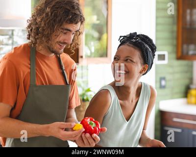 Ein vielseitiges Paar, eine junge Afroamerikanerin und ein kaukasischer Mann lachen in einer Küche Stockfoto
