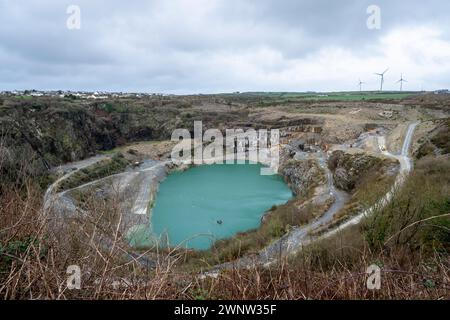 Delabole Schieferbruch mit Bergbaubaggern und Lkws. Darüber befindet sich das Dorf Delabole und auch Windräder. Delabole, Cornwall, Großbritannien. Stockfoto