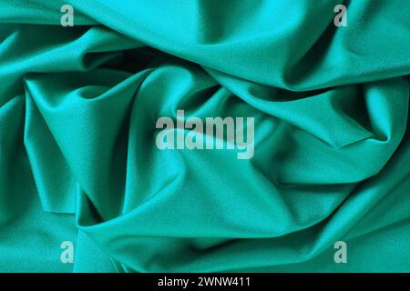 Hintergrund mit grünem Seidenstoff. Schöne Falten auf dem Material, das zur Mitte hin verdreht ist. Weicher Glanz auf dem Material Stockfoto