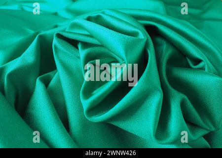 Hintergrund mit grünem Seidenstoff. Schöne Falten auf dem Material, das zur Mitte hin verdreht ist. Weicher Glanz auf dem Material Stockfoto