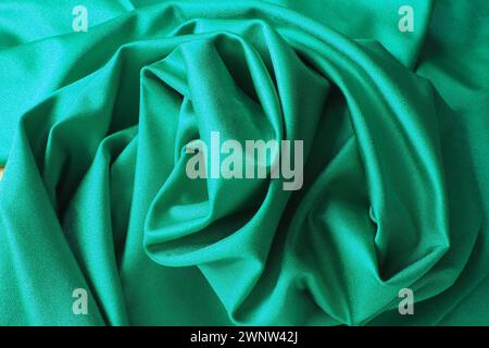Hintergrund mit grünem Seidenstoff. Schöne Falten auf dem Material, das zur Mitte hin verdreht ist. Weicher Glanz auf dem Material Stockfoto