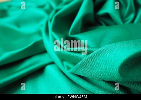 Hintergrund mit grünem Seidenstoff. Schöne Falten auf dem Material, das zur Mitte hin verdreht ist. Weicher Glanz auf dem Material Stockfoto