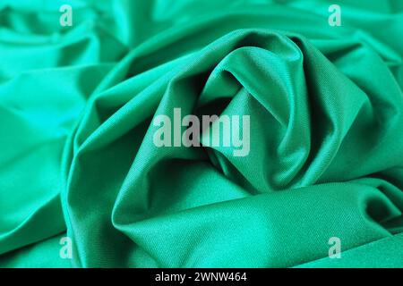 Hintergrund mit grünem Seidenstoff. Schöne Falten auf dem Material, das zur Mitte hin verdreht ist. Weicher Glanz auf dem Material Stockfoto