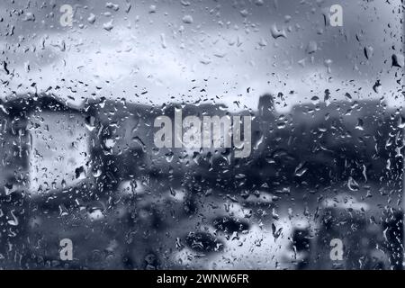 Schlechtes Wetter in der Stadt. Gebäude, Häuser, Autos vor dem Fenster. Trübungs-Cumulus-Wolken. Meteorologie und Wettervorhersage. Regentropfen laufen herunter Stockfoto