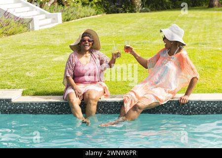 Eine ältere afroamerikanische Frau lacht mit einem Freund am Pool, der beide Getränke hält Stockfoto