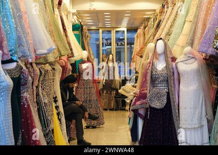 Ein Mann sitzt in seinem Kleiderladen und verkauft südasiatische Kleider in Southall, West London Stockfoto