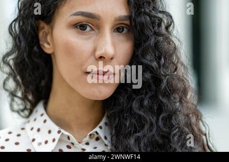 Nahaufnahme einer eleganten Frau mit lockigem Haar in einer stylischen Polka-Dot-Bluse. Das Bild zeigt ein modisches weibliches Detail, das perfekt für Beauty- und Modeschöpfe geeignet ist. Stockfoto