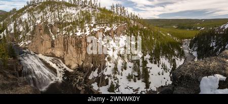 Ein bezauberndes Bild eines mächtigen Wasserfalls, der durch eine schneebedeckte Landschaft stürzt und durch die zerklüfteten Klippen, umgeben von Kiefern, schneidet Stockfoto