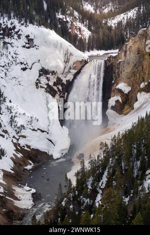 Ein bezauberndes Bild eines mächtigen Wasserfalls, der durch eine schneebedeckte Landschaft stürzt und durch die zerklüfteten Klippen, umgeben von Kiefern, schneidet Stockfoto