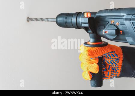 Arbeiter Hand mit einem Bohrhammer. Hände in Schutzhandschuhen mit Hammerbohrer-Perforator. Nahaufnahme Stockfoto