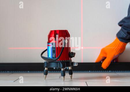 Arbeiter und Blase, Laserpegel. Linien an der Wand. Messen mit rotem Laserpegel. Messgenauigkeit Konzept, moderne Messgeräte Stockfoto