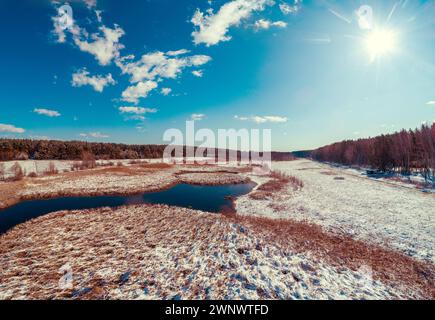 Aus der Vogelperspektive auf den sich windenden Fluss im frühen Frühjahr. Schnee liegt auf trockenem Schilf Stockfoto