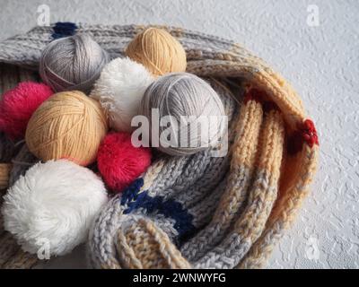 Garn, Garn, warmer Schal auf weiß-grauem Hintergrund. Stricken als Hobby. Weißes, beigefarbenes, graues, rotes Subest und Wollgarn Stockfoto