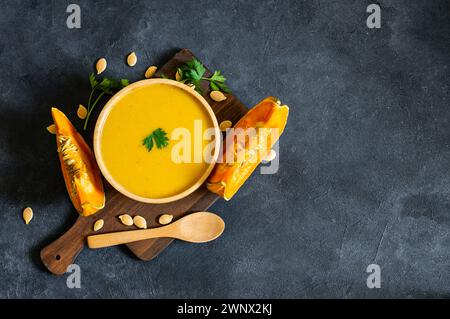 Hausgemachte Kürbis-Karottensuppe mit Petersilie in der Schüssel und frischen Kürbissen auf rustikalem Hintergrund Stockfoto
