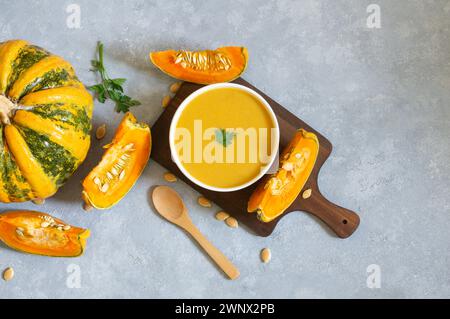 Hausgemachte Kürbis-Karottensuppe mit Petersilie in der Schüssel und frischen Kürbissen auf rustikalem Hintergrund Stockfoto